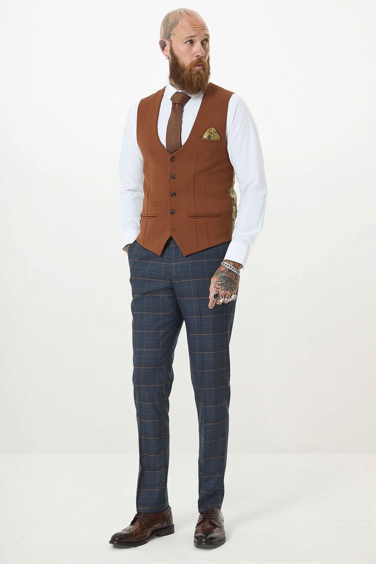 A bearded, bald man with hand tattoos models the marcdarcy JENSON Marine Navy Check Suit with Kelvin Tan Waistcoat against a white background, styled with a white shirt, brown tie, pocket square, and brown shoes.