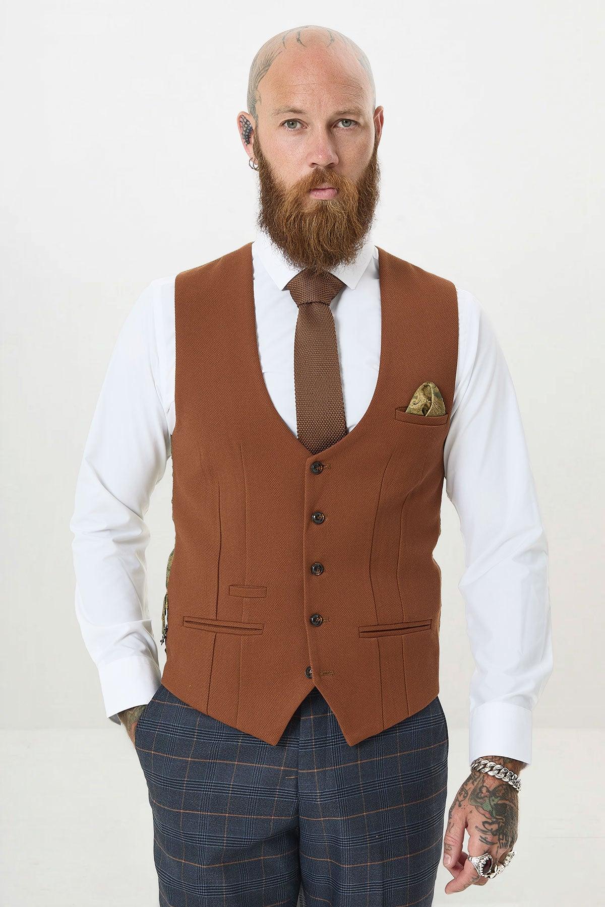 A bearded man with tattoos wears the marcdarcy JENSON Marine Navy Check Suit with Kelvin Tan Waistcoat over a white shirt and tie, standing against a plain light background and looking directly at the camera.