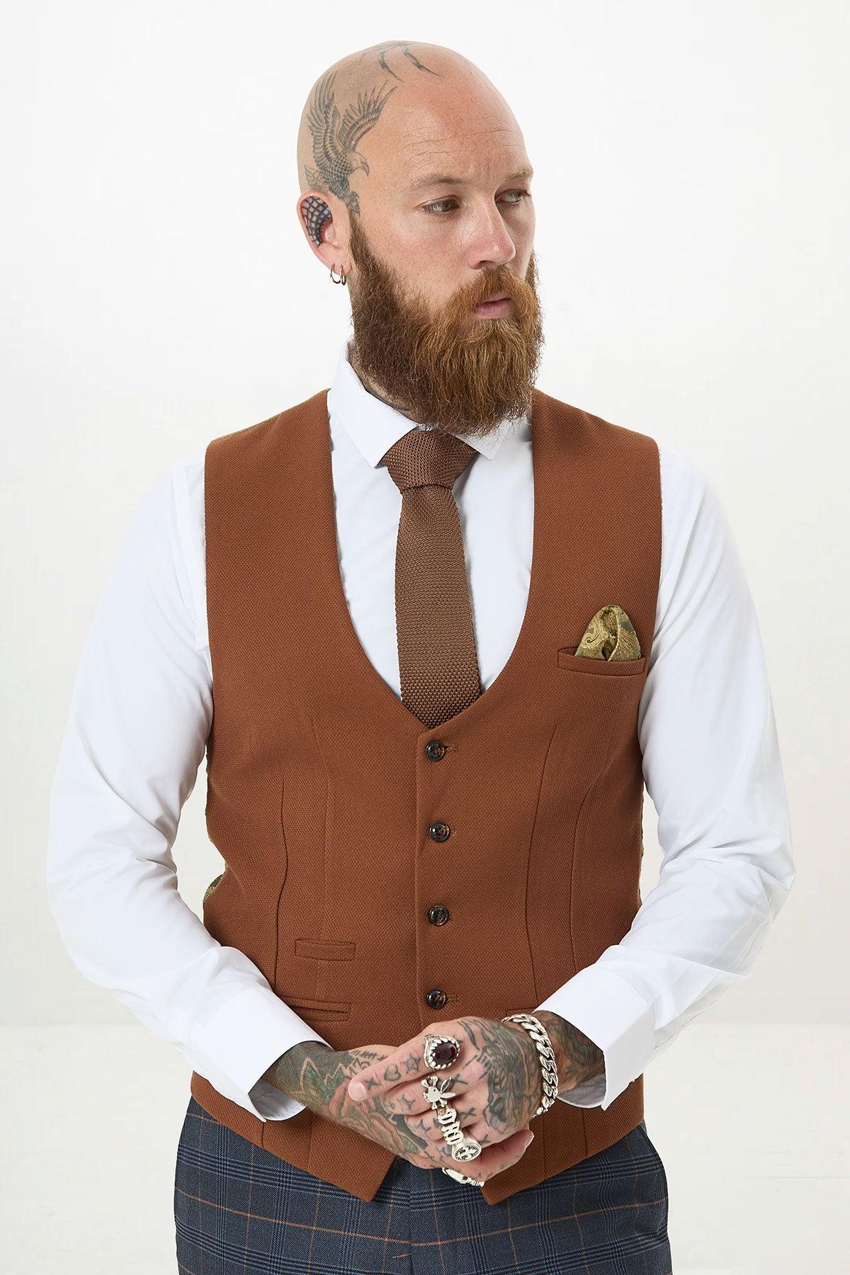 A bearded man with tattoos and piercings models the marcdarcy JENSON Marine Navy Check Suit with Kelvin Tan Waistcoat, accessorized with rings and bracelets, gazing to the side against a plain light background.