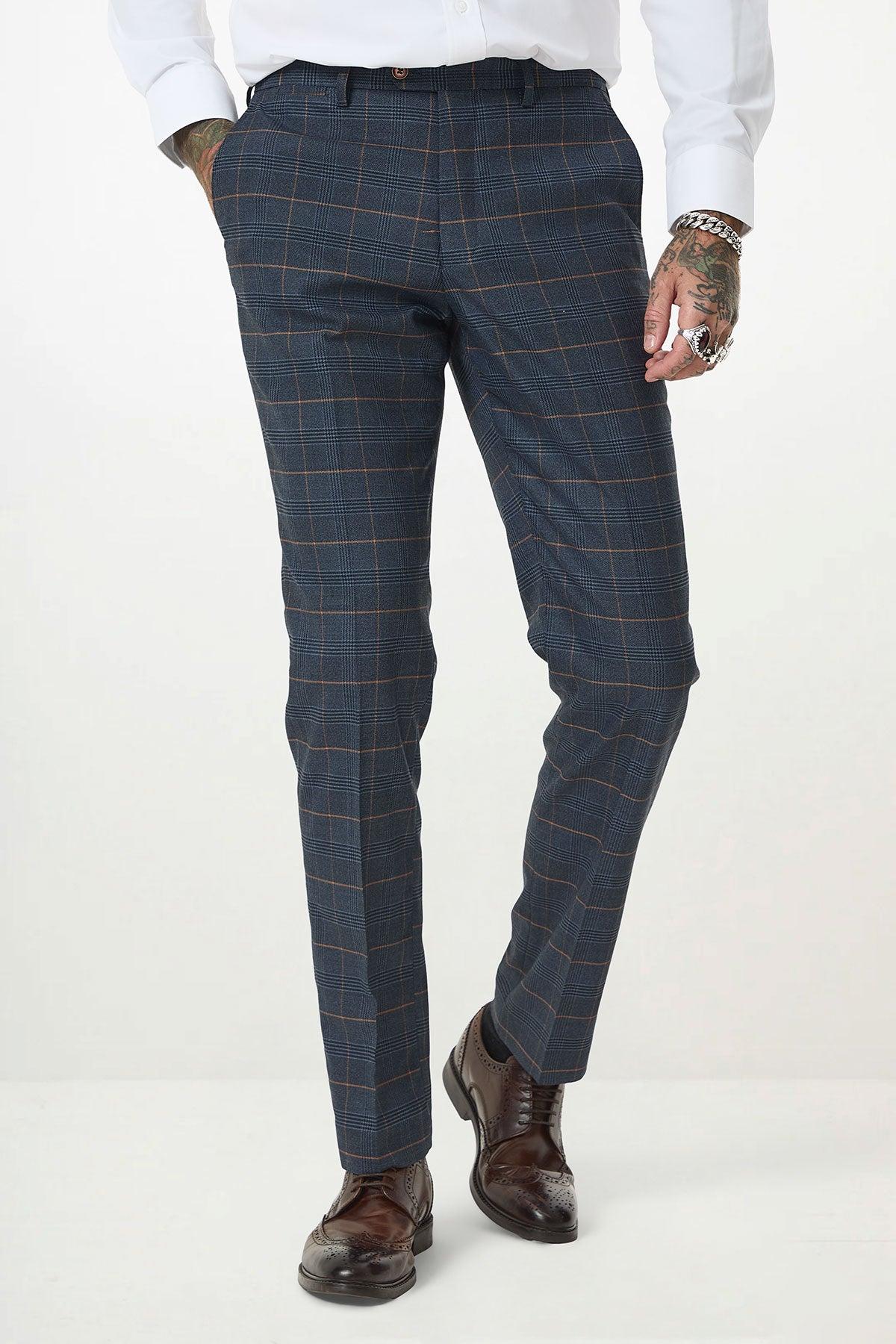 A person wearing the marcdarcy JENSON - Marine Navy Check Suit with Kelvin Tan Waistcoat, a white shirt, and brown shoes. Visible tattoos, rings, and a watch; hands in pockets. Photo shows them from shoulders down.