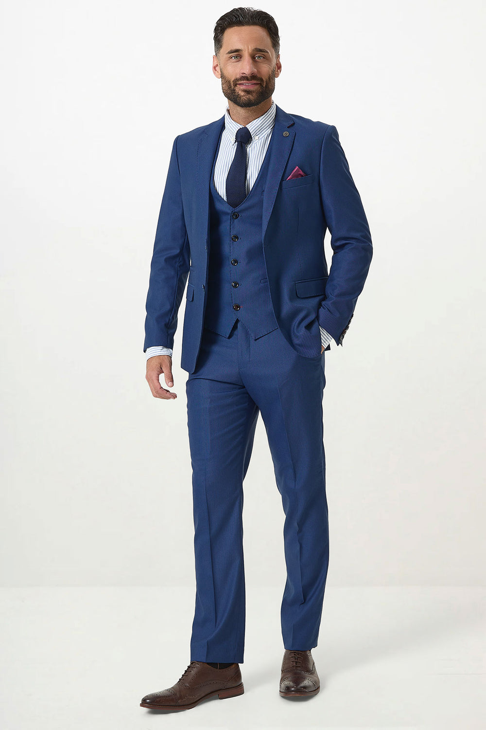 A man wears the Marc Darcy DANNY Royal Blue Three Piece Suit with a single-breasted waistcoat, styled with a white striped shirt, navy tie, and brown shoes. He stands against a white background, embodying classic workwear elegance.