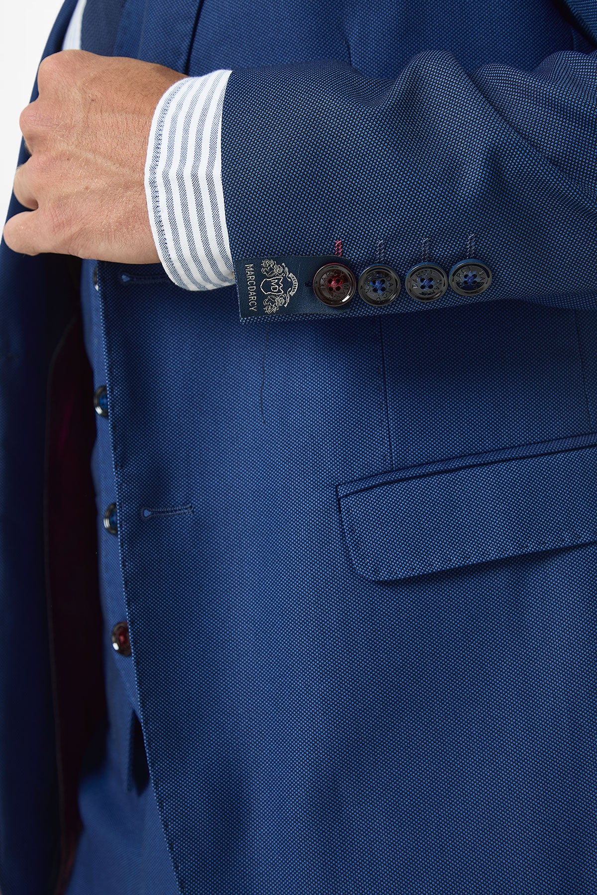 A close-up of a person adjusting the Marc Darcy DANNY Royal Blue Two Piece Suit, featuring a slim fit and four buttons on the sleeve, worn over a white shirt with blue stripes.