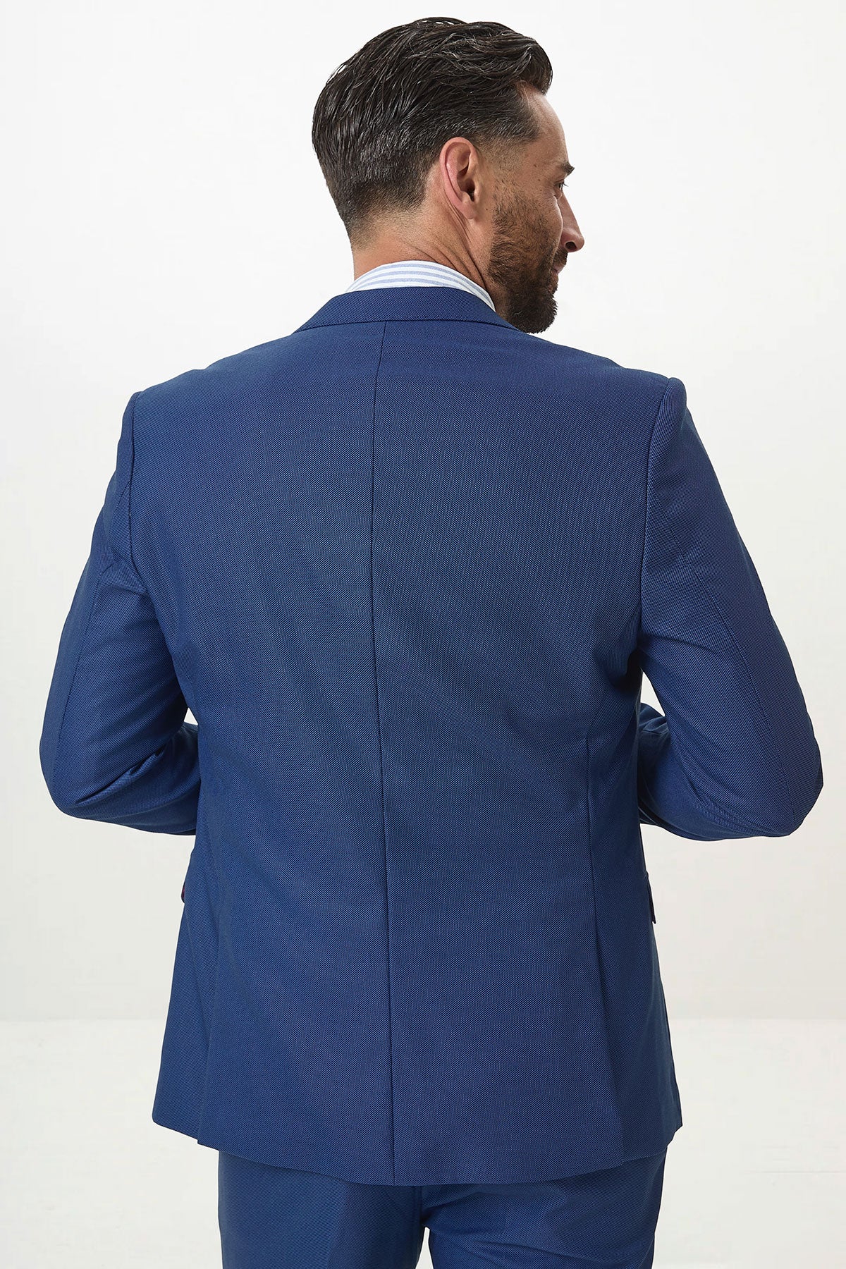 A man with short dark hair, wearing a Marc Darcy DANNY Royal Blue Tailored Blazer from his workwear wardrobe, stands with his back to the camera in a well-lit studio.