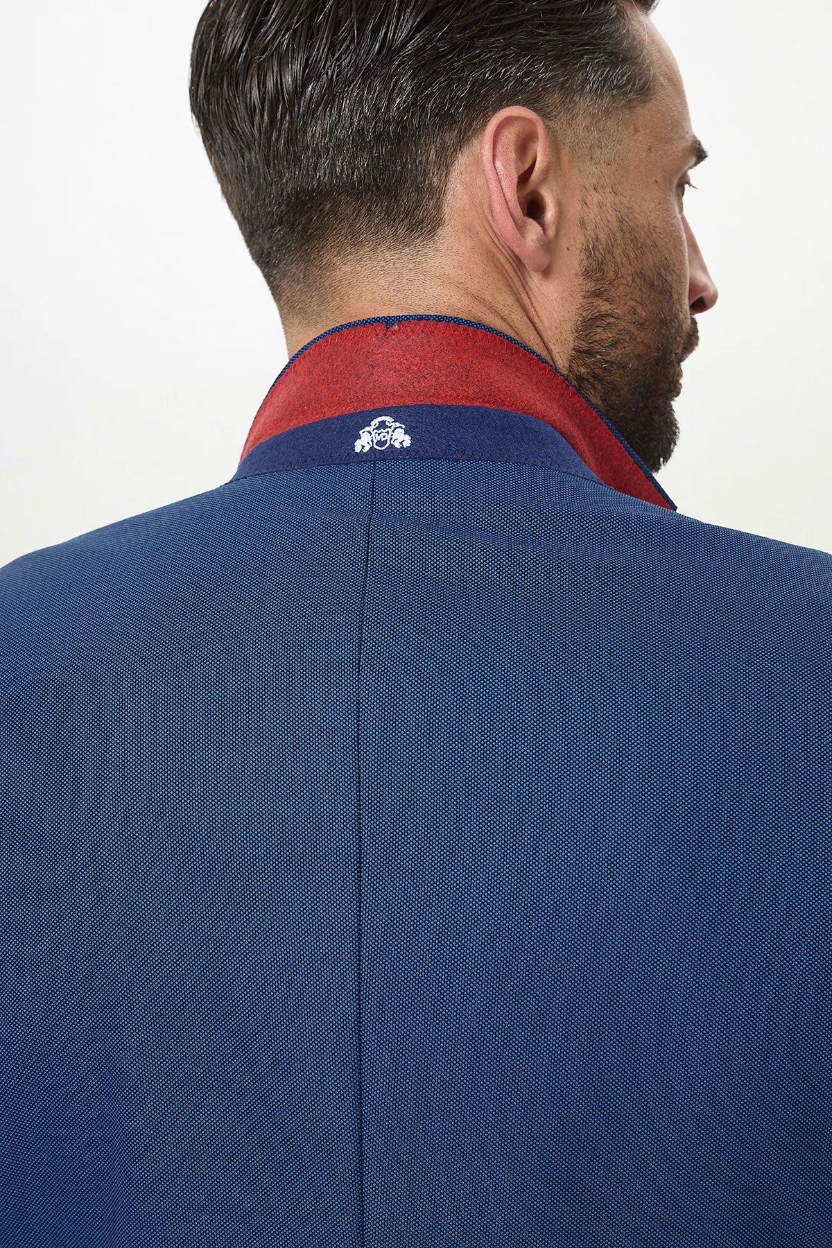 A man seen from behind wears the Marc Darcy DANNY - Royal Blue Tailored Blazer with the collar turned up, revealing a red inner lining and white embroidery—a stylish slim-fit choice for any workwear wardrobe.