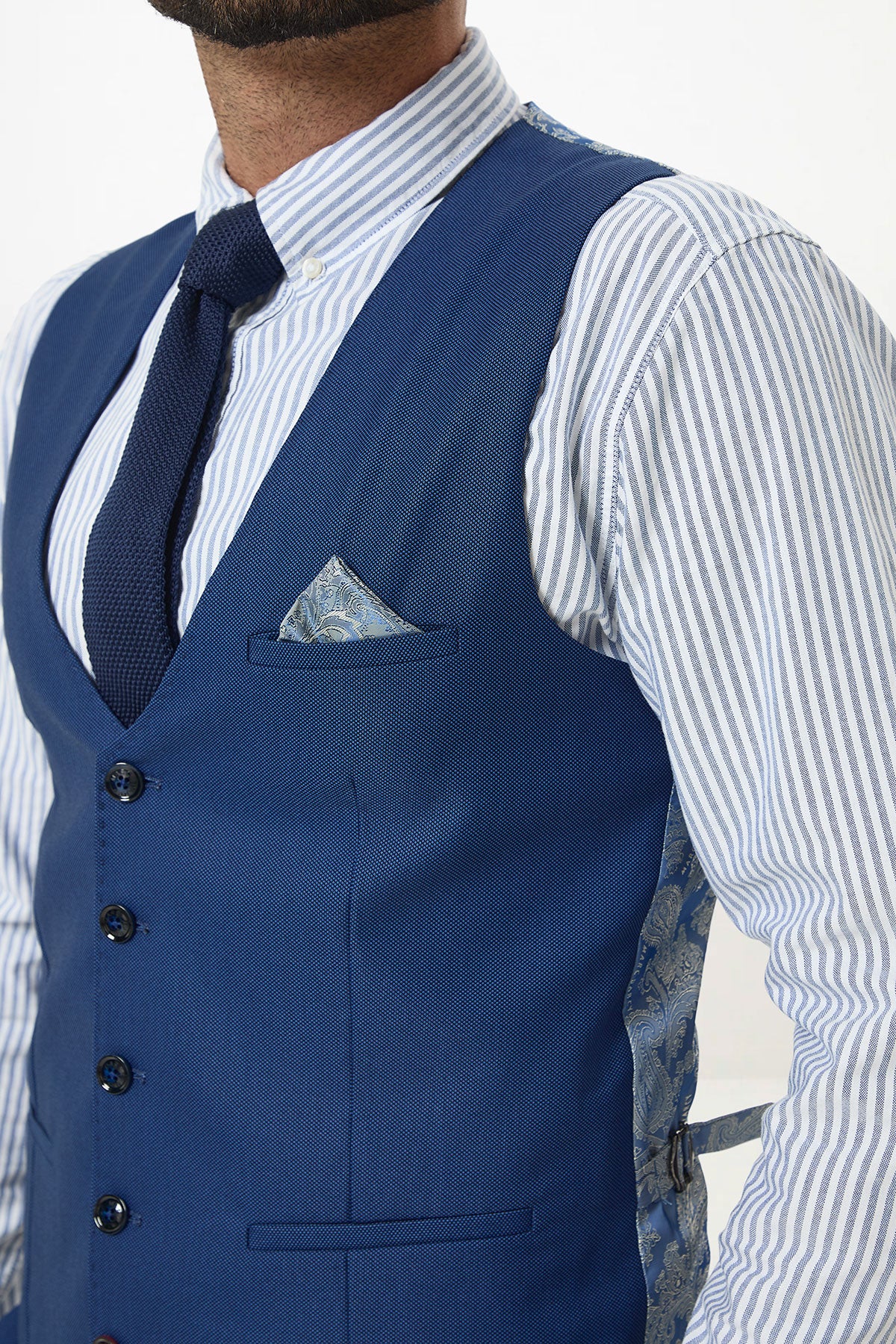 A man wears the Marc Darcy DANNY Royal Blue Single Breasted Waistcoat with a striped shirt, navy tie, and patterned pocket square.