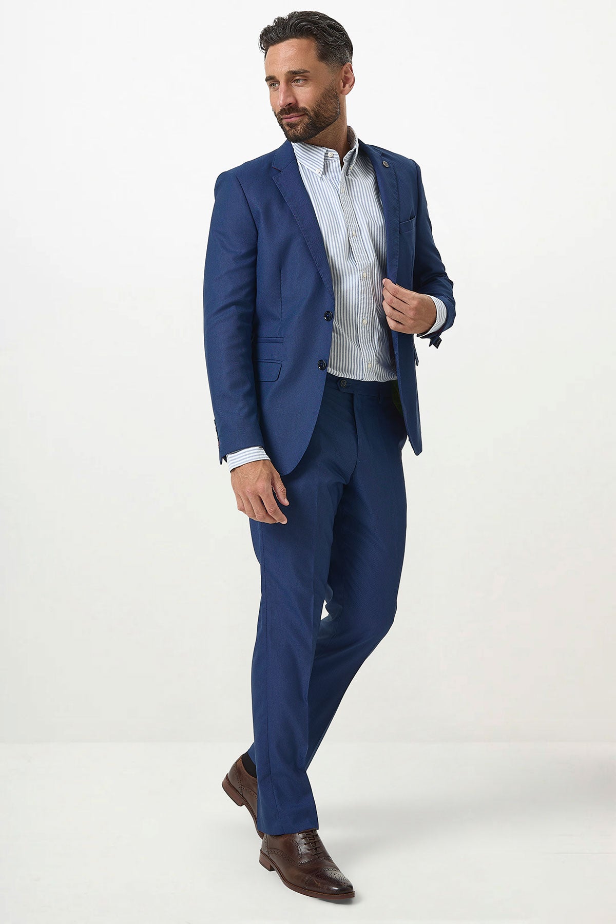 A man with short dark hair and a beard poses against a white background wearing the Marc Darcy DANNY Royal Blue Two Piece Suit, styled with a light striped dress shirt and brown dress shoes.