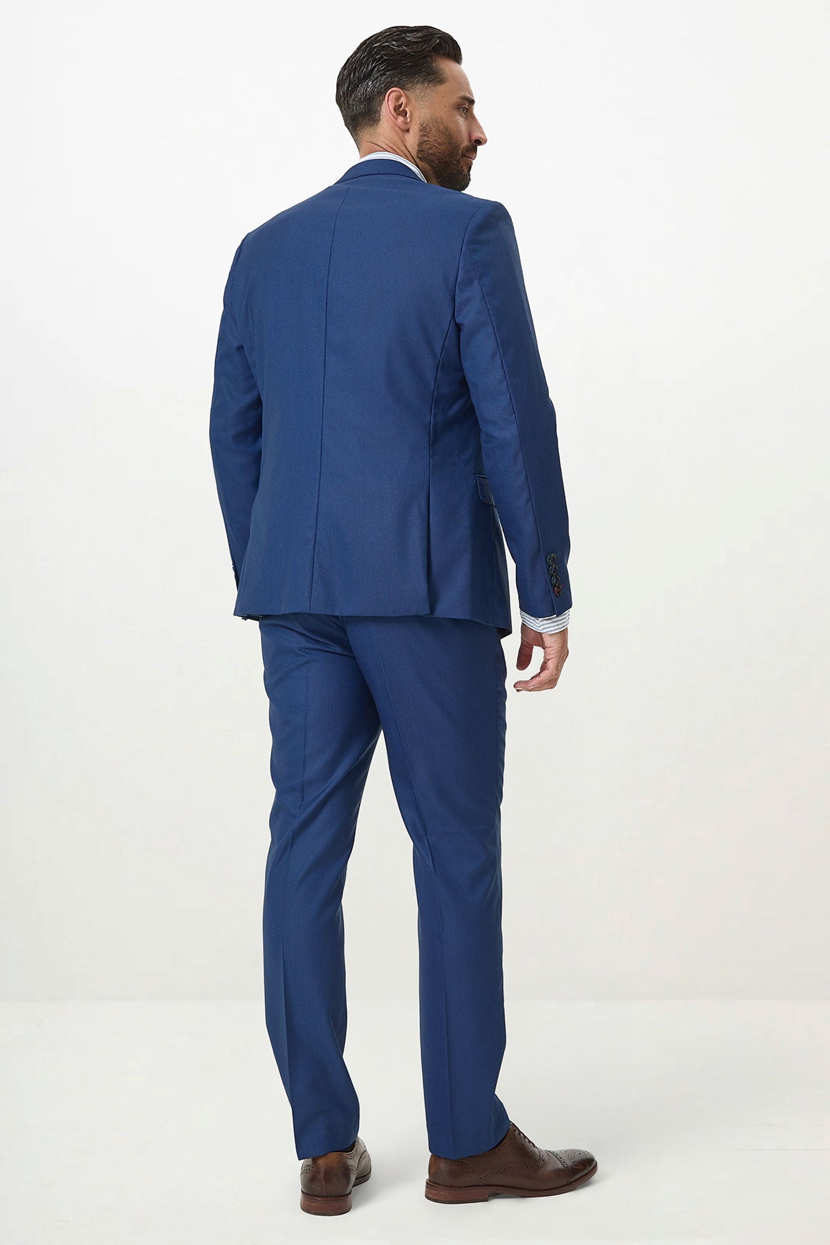A man models the Marc Darcy DANNY Royal Blue Two Piece Suit with a light blue shirt and brown shoes, standing against a plain white background, facing away and slightly turned to the right.