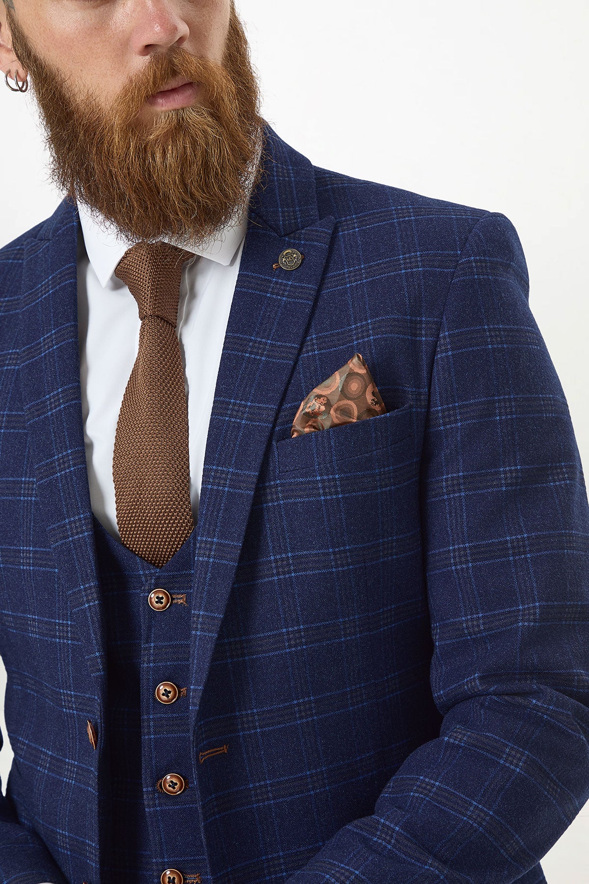 A bearded man wears the marcdarcy CHIGWELL Blue Tweed Check Blazer, white shirt, brown textured tie, and brown patterned pocket square, gazing to the side. The slim fit blazer adds a modern touch to his formal look.