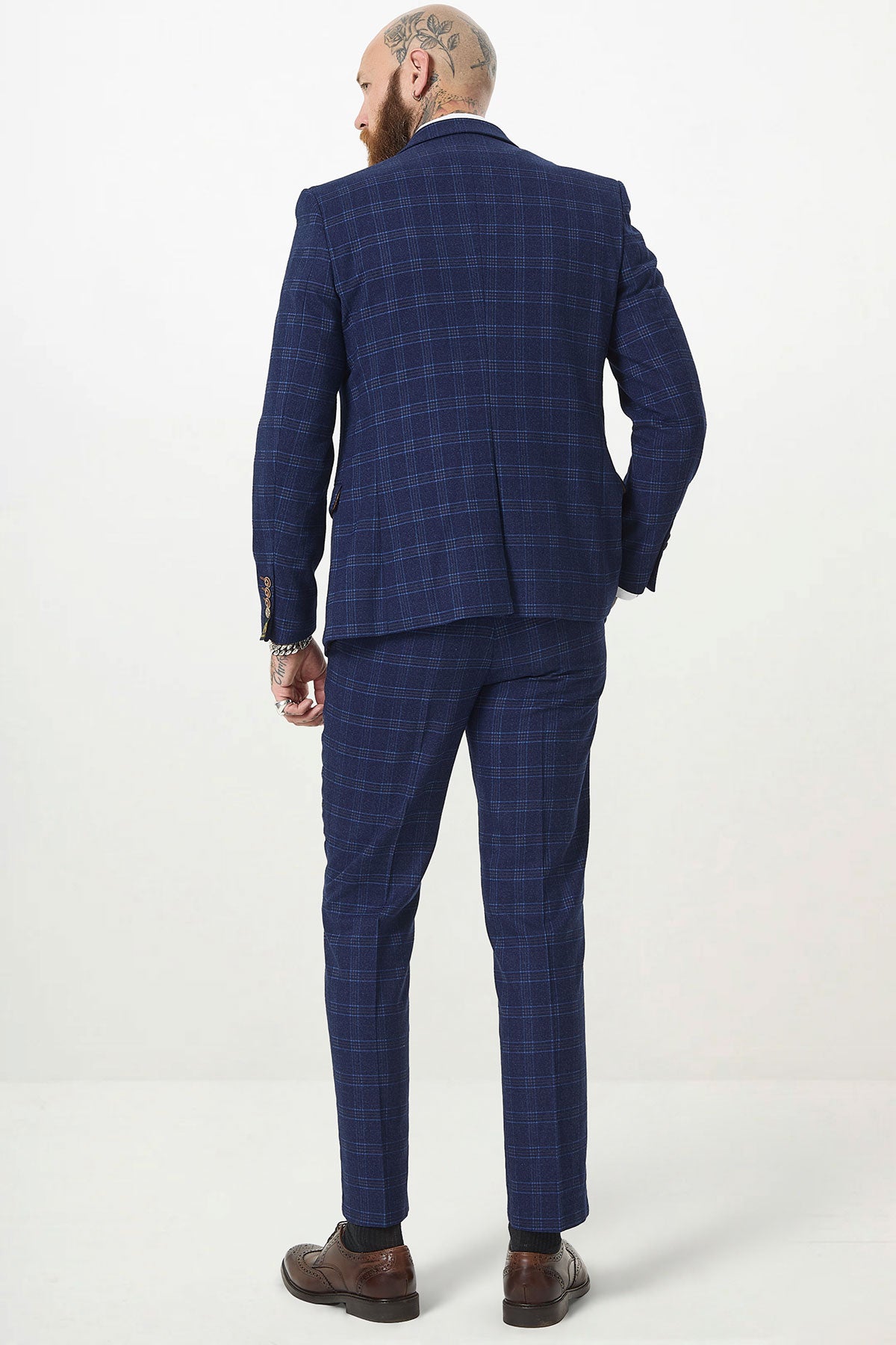 A bald, tattooed person is seen from behind in a marcdarcy CHIGWELL Blue Tweed Check Three Piece Suit with matching pants and brown shoes, standing against a plain white background.