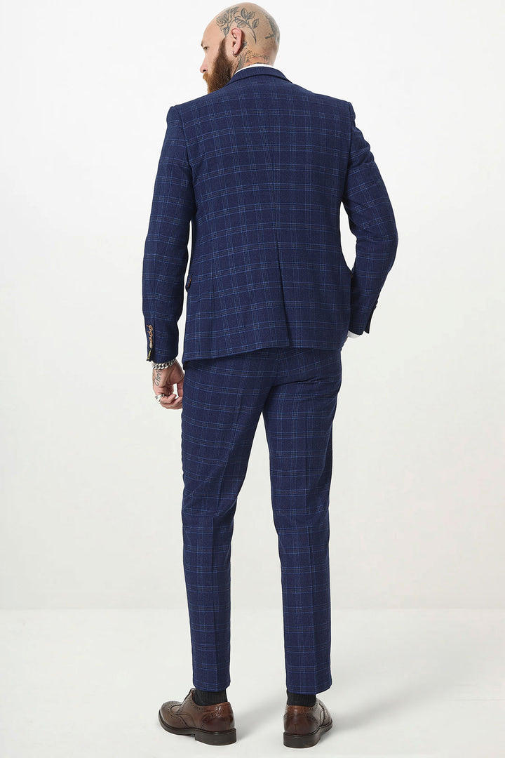 A man with tattoos and a beard wears the marcdarcy CHIGWELL Blue Tweed Check Three Piece Suit and brown shoes, standing with his back to the camera against a plain white background.