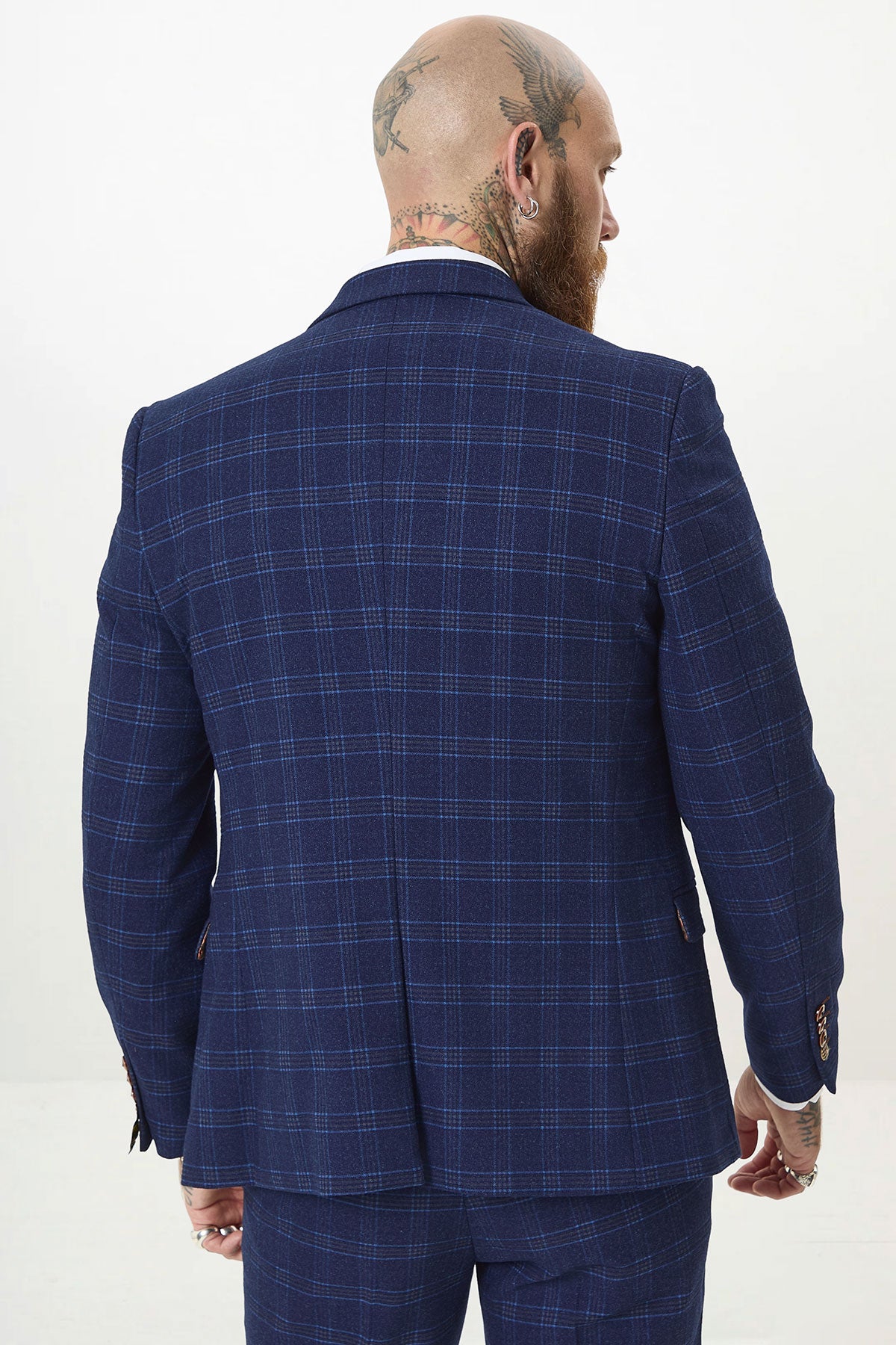 A man with tattoos on his bald head and beard is seen from behind, wearing the marcdarcy CHIGWELL Blue Tweed Check Blazer and matching trousers, standing against a plain white background.