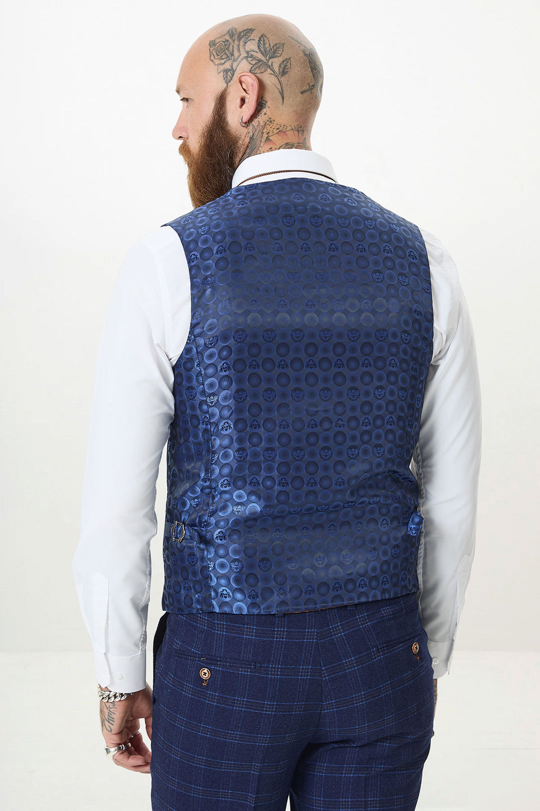 A man with a tattooed bald head and beard is seen from the back, wearing the marcdarcy CHIGWELL Blue Tweed Check Three Piece Suit—featuring a blue check waistcoat with a shiny circular pattern, white shirt, and plaid trousers. Perfect for formal events.