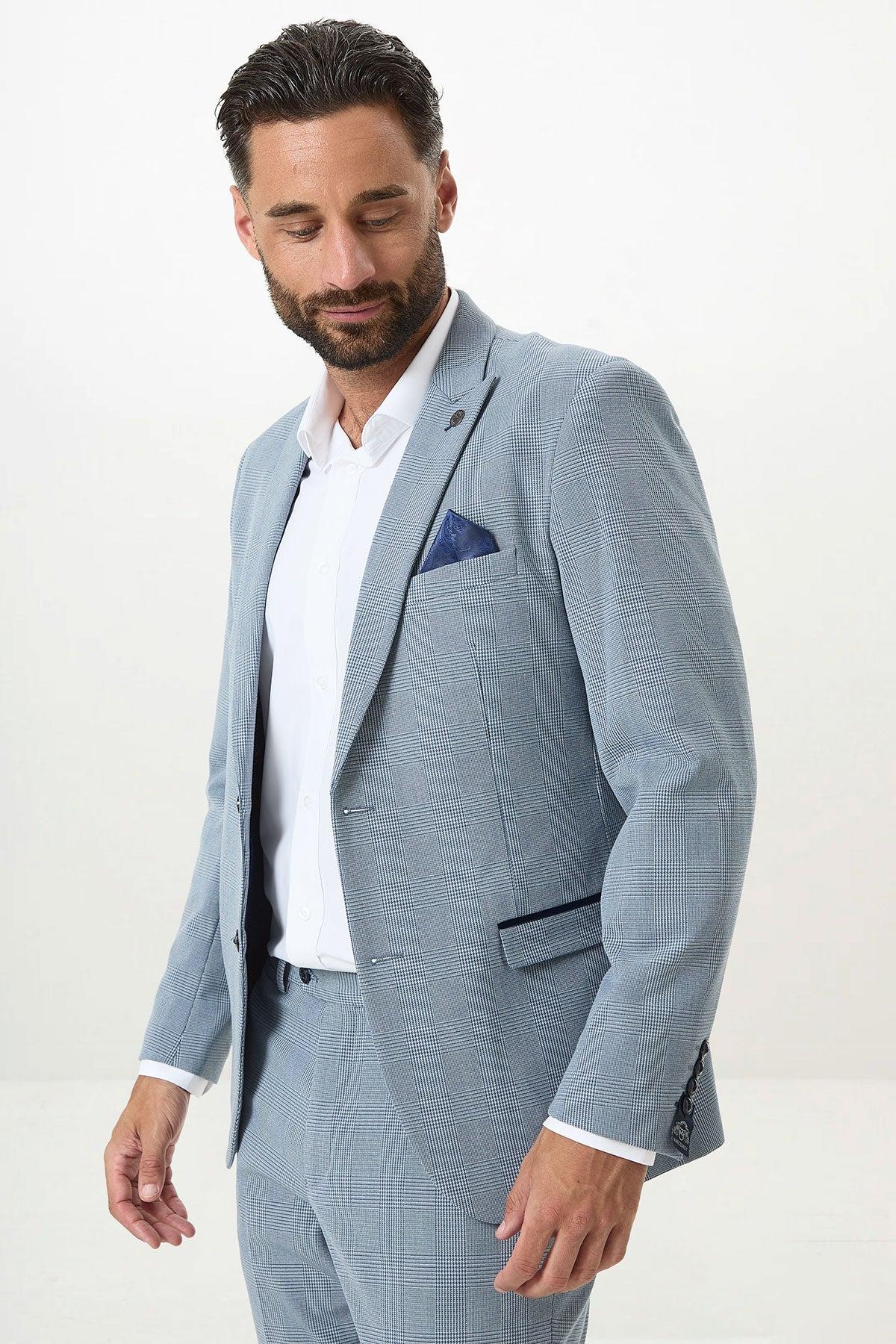 A man with dark hair and a beard wears the Marc Darcy BROMLEY Sky Blue Check Two Piece Suit with a white shirt and navy pocket square, looking down against a plain white background.