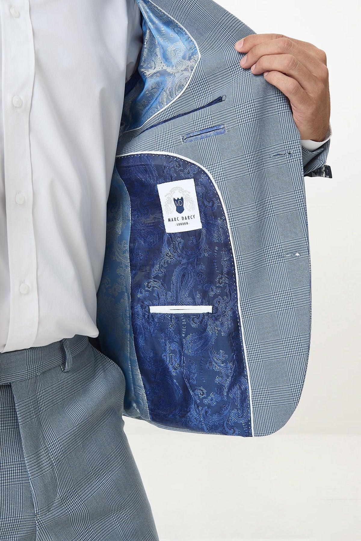 A person in a Marc Darcy BROMLEY Sky Check Suit with Kelvin Royal Waistcoat holds open the jacket, revealing a shiny blue paisley lining and Marc Darcy label. The look is finished with a crisp white dress shirt.