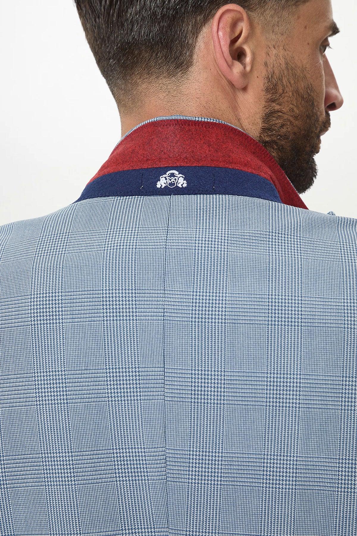 A close-up of a man wearing the Marc Darcy BROMLEY - Sky Check Suit with Kelvin Sky Waistcoat. The jacket’s collar is turned up, showing a red and navy lining and small white logo. His short brown hair and beard are visible.