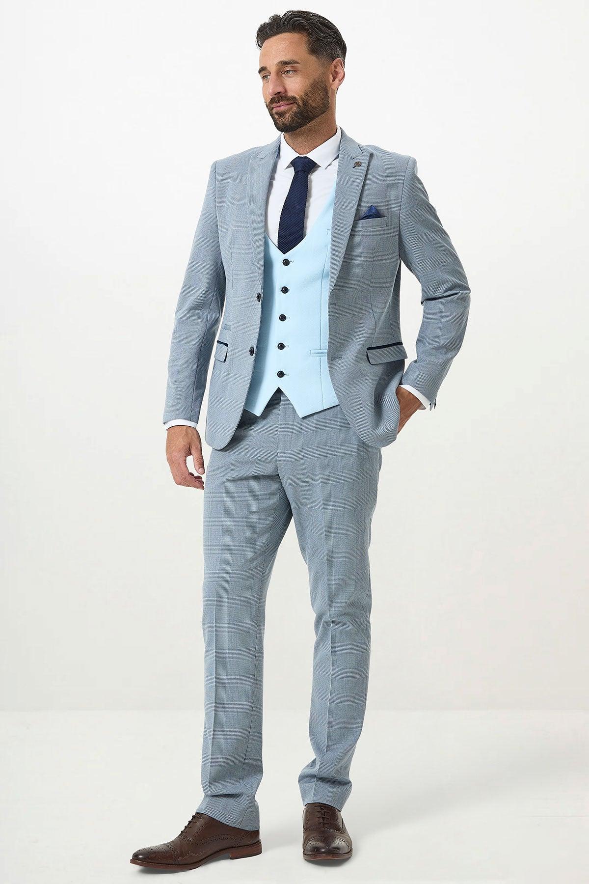 A man with short dark hair and a beard wears the Marc Darcy BROMLEY - Sky Check Suit with Kelvin Sky Waistcoat, styled with a white shirt, dark tie, and brown shoes, standing against a plain light background.