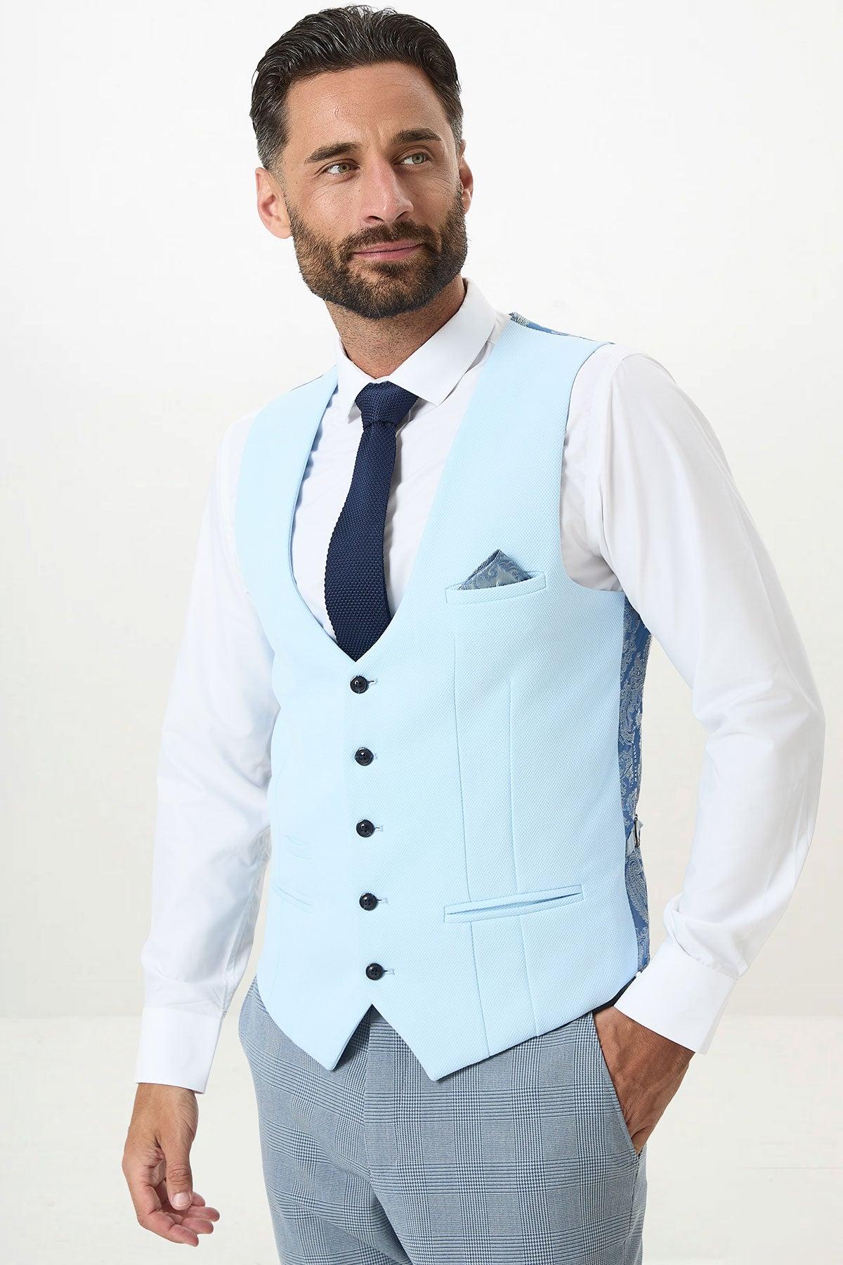 A man wears the marcdarcy KELVIN Sky Blue Single Breasted Waistcoat with a white shirt, navy tie, plaid pants, and a patterned pocket square.