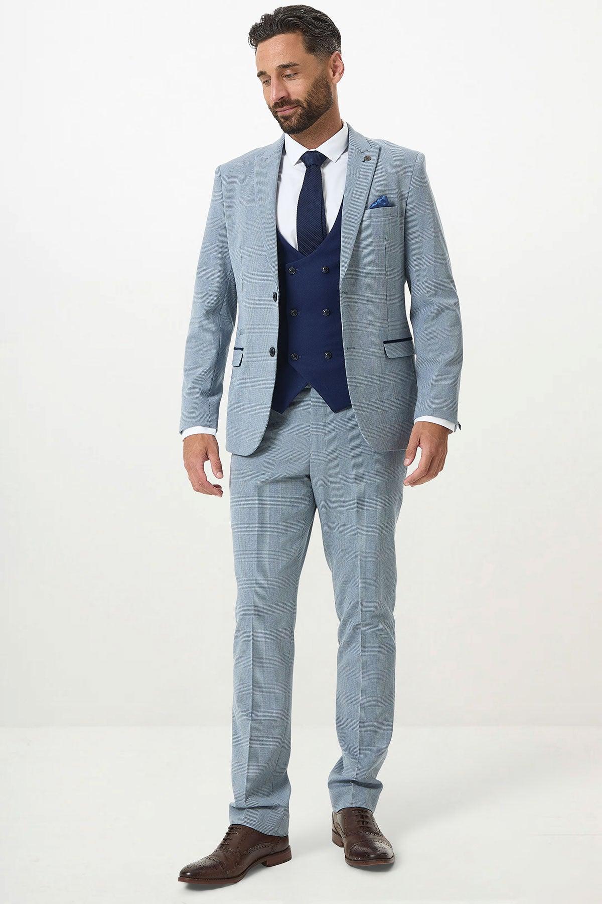 A man with short dark hair and a trimmed beard wears the Marc Darcy BROMLEY Sky Check Suit with Kelvin Royal Waistcoat, paired with a white shirt, blue tie, and brown shoes against a plain white background.