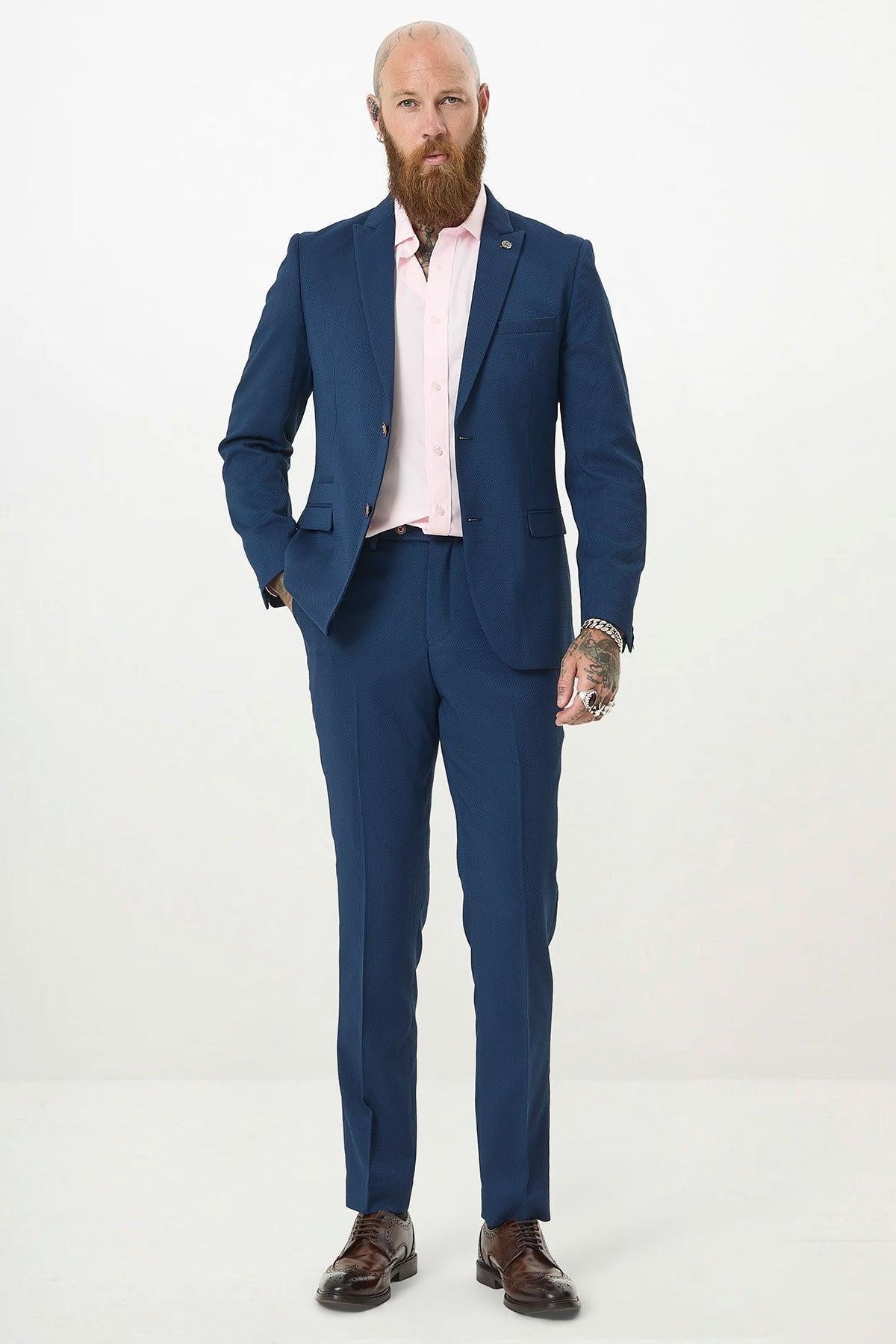 A man with a beard, wearing the marcdarcy MAX - Royal Blue Blazer with Contrast Buttons, a light pink dress shirt, and brown shoes stands against a plain white background—an ideal office wear look.