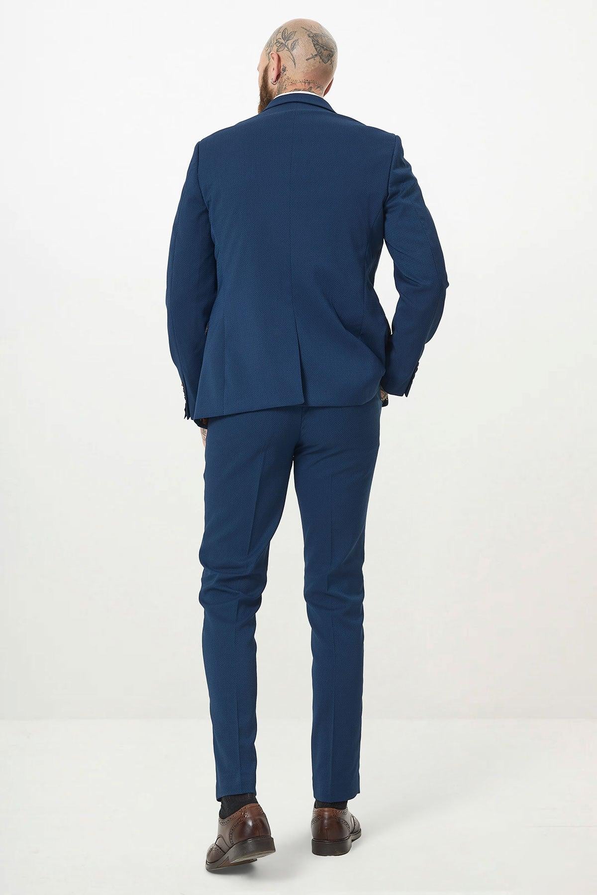 A bald man with tattoos on his head, dressed in the Marc Darcy MAX Royal Blue Two Piece Suit and brown shoes, stands with his back to the camera against a plain white background.