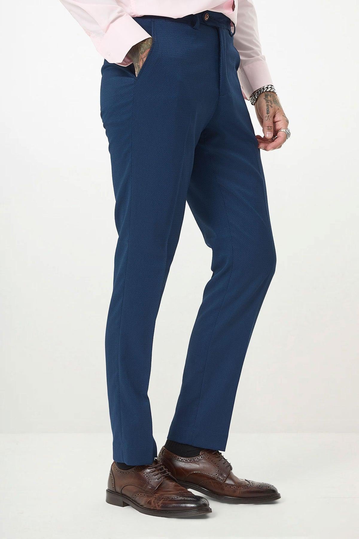 A person in marcdarcy’s MAX Royal Blue Trousers with contrast buttons, a light pink shirt, brown leather dress shoes, and bracelets stands against a white background. Only the lower body and one hand are visible—perfect for stylish office wear.