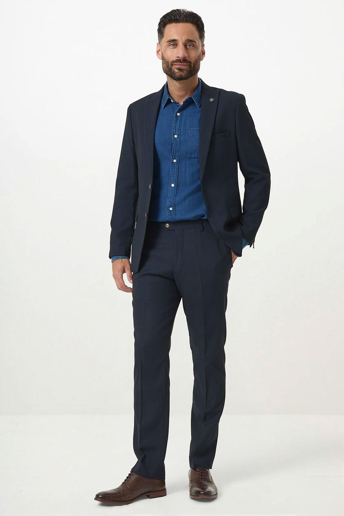 A man with short dark hair and a beard wears the Marc Darcy MAX Navy Blue Two Piece Suit, paired with a blue shirt and brown dress shoes, standing against a plain white background.