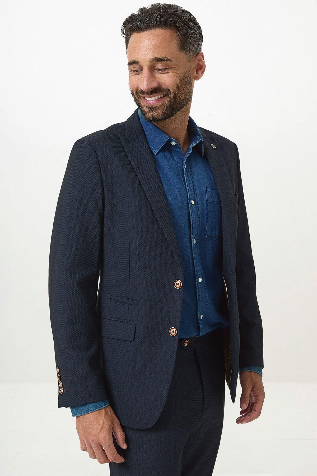 A smiling man wears the marcdarcy MAX - Navy Blue Blazer with Contrast Buttons over a denim shirt, paired with matching navy trousers—modern office style, set against a white background.