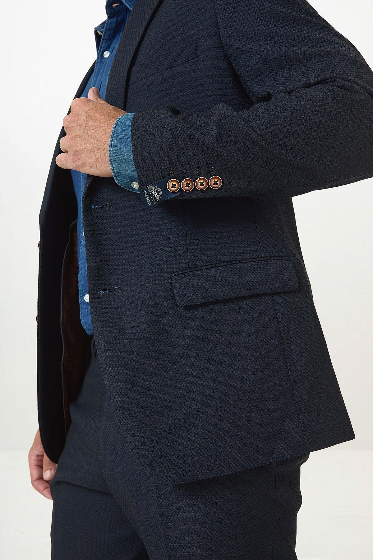 A person in the marcdarcy MAX Navy Blue Blazer with contrast buttons adjusts their jacket, showing off the brown buttons and a hint of inner lining. The plain light background highlights this perfect office wear style.