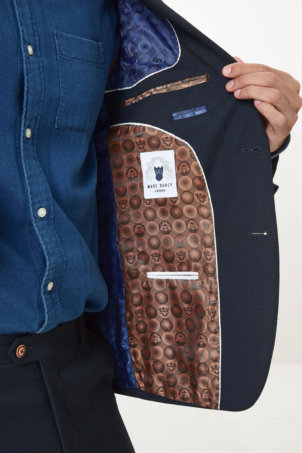 A person in a blue shirt and dark trousers holds open the marcdarcy MAX - Navy Blue Blazer with Contrast Buttons, revealing its brown patterned lining and visible label—ideal for stylish office attire.