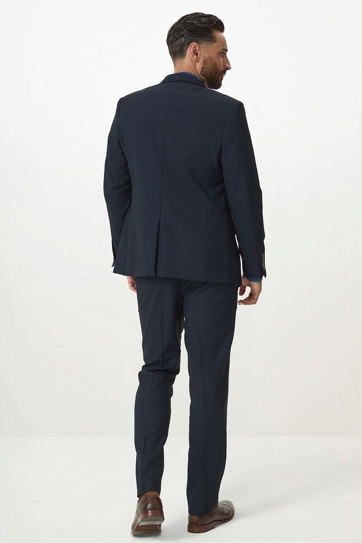 A man with dark hair and a beard faces away from the camera, wearing the marcdarcy MAX Navy Blue Blazer with Contrast Buttons—ideal for office wear—with brown shoes, all set against a plain white background.