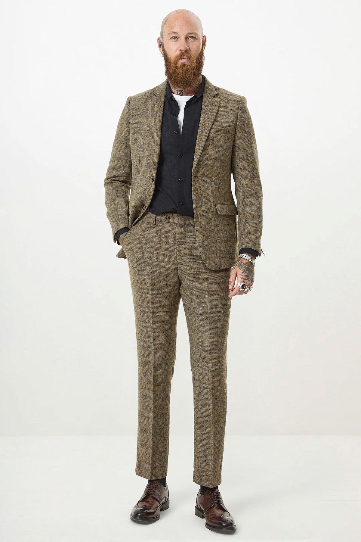 A bald man with a full beard wears the marcdarcy KRIS Tan Tweed Two Piece Suit in a slim fit with a black shirt, displaying tattoos and jewelry.