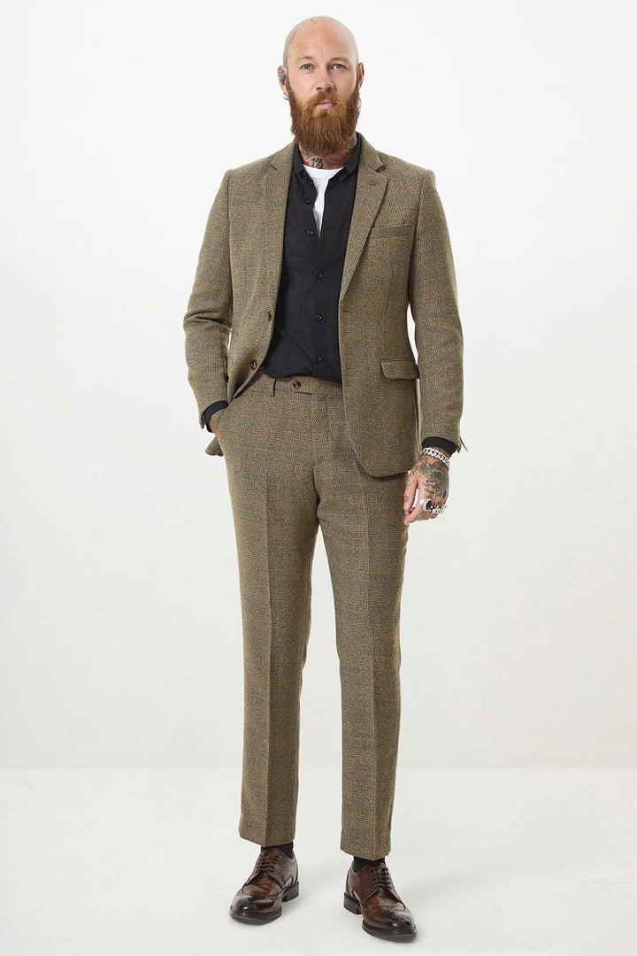 A bald man with a full beard wears the marcdarcy KRIS Tan Tweed Two Piece Suit in a slim fit with a black shirt, displaying tattoos and jewelry.