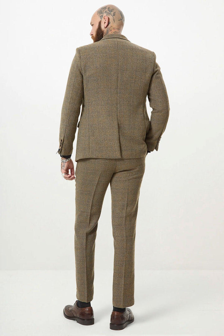 A man with a shaved, tattooed head faces away from the camera, wearing the marcdarcy KRIS Tan Tweed Two Piece Suit and brown dress shoes against a plain light background.