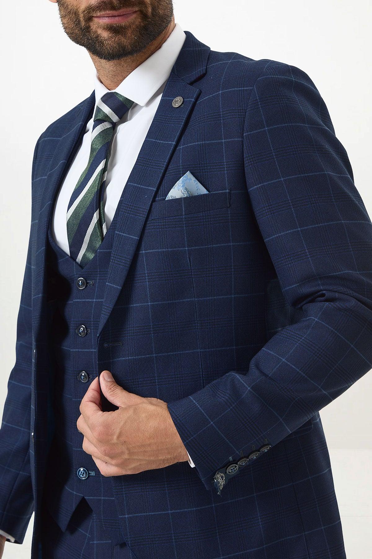 A man in the Marc Darcy EDINSON Navy Sky Check Two Piece Suit with matching vest, white shirt, striped tie, and light blue pocket square holds his jacket; image is cropped above the mouth.
