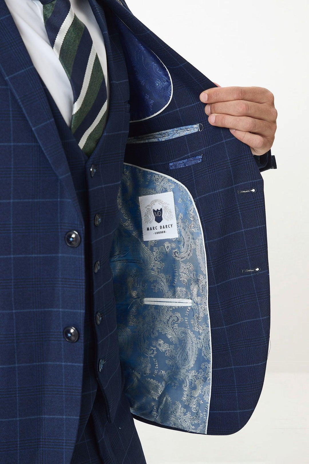 A man in a slim tailored Marc Darcy EDINSON Navy Sky Check Blazer and striped tie opens his jacket to reveal its light blue paisley-patterned lining and the Marc Darcy label inside.