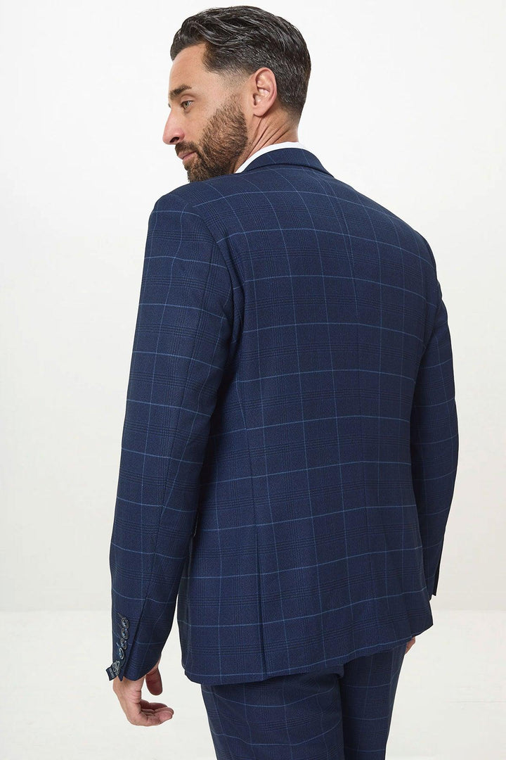 A man with dark hair and a beard models the Marc Darcy EDINSON - Navy Sky Check Blazer, slim tailored fit, turned slightly away to show the back and side of the suit against a plain white background.
