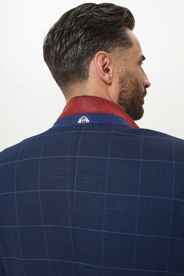 A man with short dark hair and a beard is seen from behind wearing the Marc Darcy EDINSON Navy Sky Check Blazer with a raised collar, featuring a red inner lining and small white embroidery.