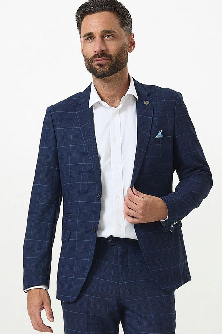A dark-haired, bearded man wears the Marc Darcy EDINSON Navy Sky Check Blazer in a slim tailored fit, paired with a white dress shirt and blue pocket square, posing confidently against a plain white background.