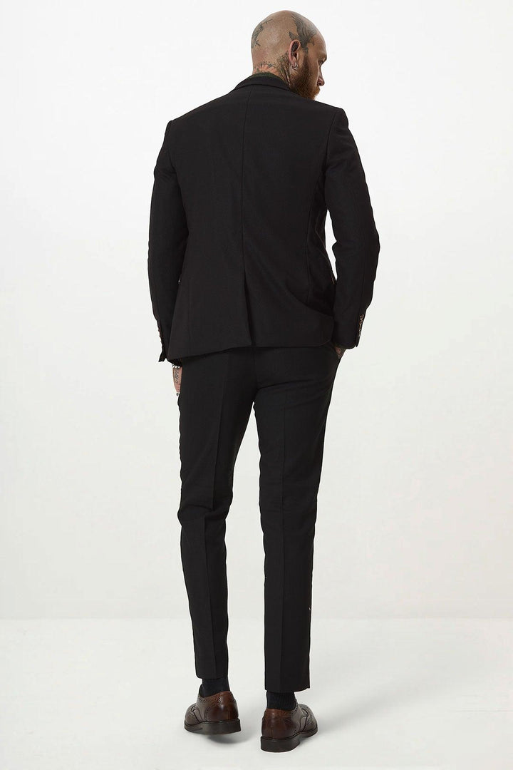 A bald, tattooed man stands facing away against a plain white background, wearing the marcdarcy MAX Black Two Piece Suit with brown shoes and a camouflage print pocket square for added flair.