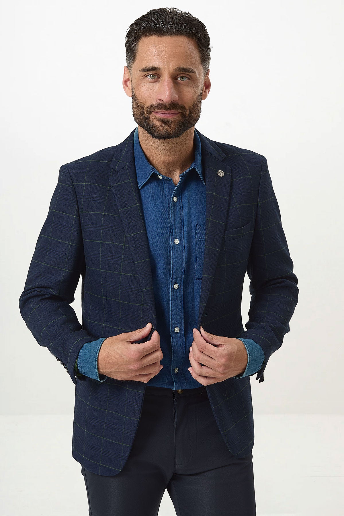 A man with dark hair and a beard wears the Marc Darcy EDINSON Navy Green Check Blazer over a blue denim shirt and dark pants, standing against a plain white background, looking at the camera with a slight smile.