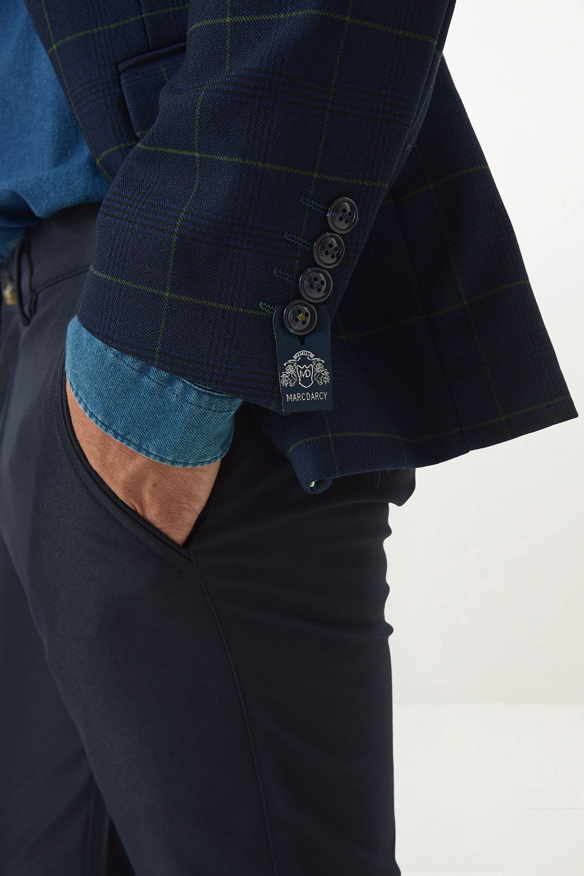 Close-up of a man wearing the Marc Darcy EDINSON Navy Green Check Blazer with a denim shirt and dark trousers, his hand in his pocket drawing attention to the blazer's slim fit and signature cuff tag.