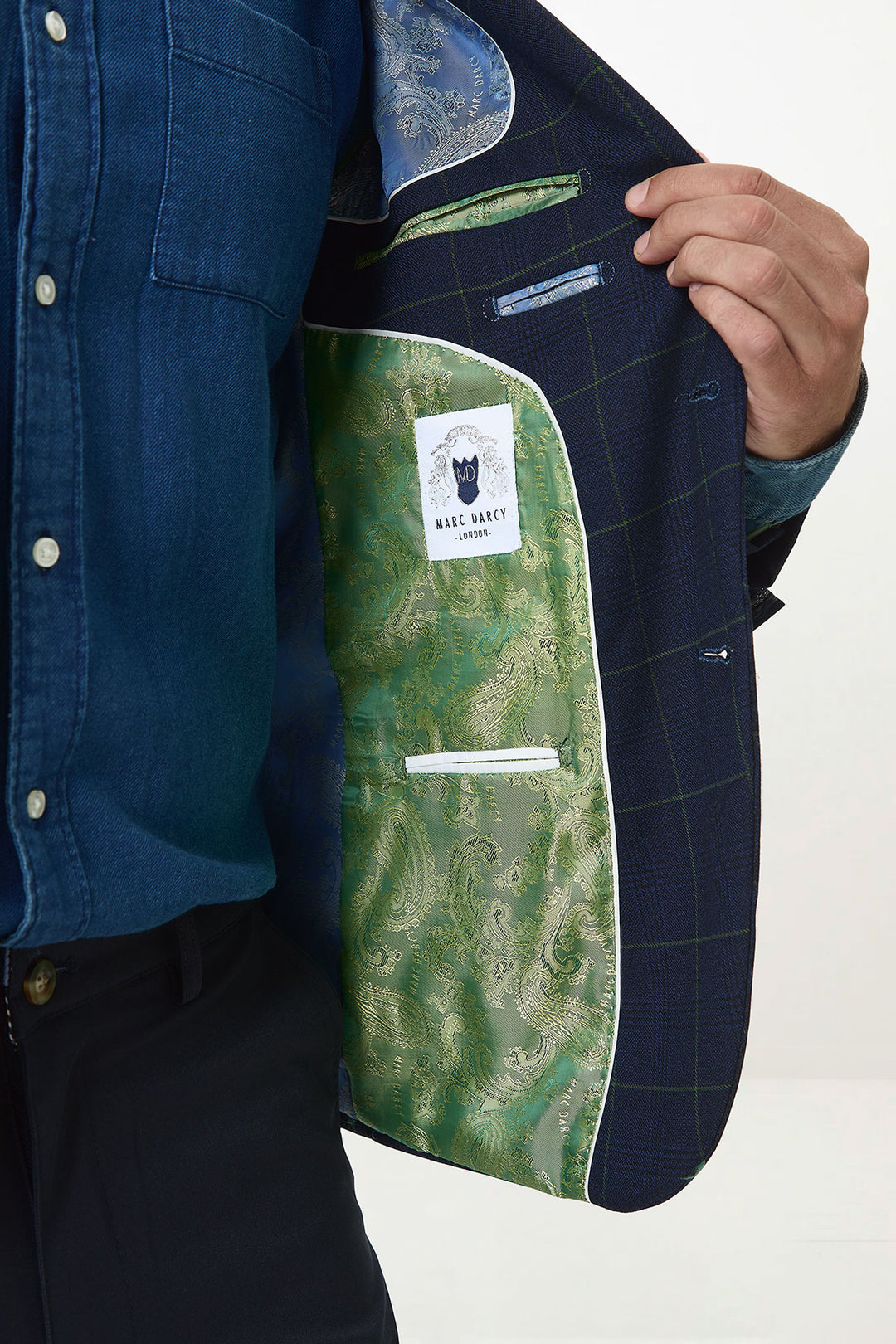 A person in a blue shirt and dark trousers holds open the Marc Darcy EDINSON navy green check blazer, revealing its green paisley-patterned satin lining with a visible Marc Darcy label inside.