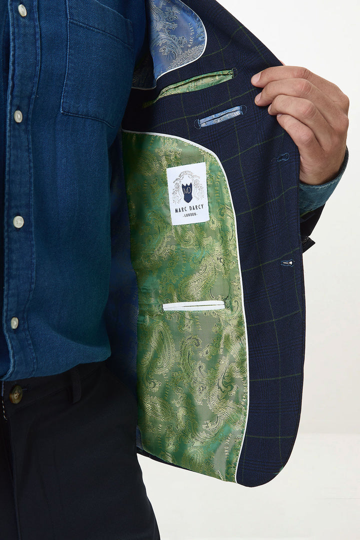 A person in a blue shirt and dark trousers holds open the Marc Darcy EDINSON navy green check blazer, revealing its green paisley-patterned satin lining with a visible Marc Darcy label inside.