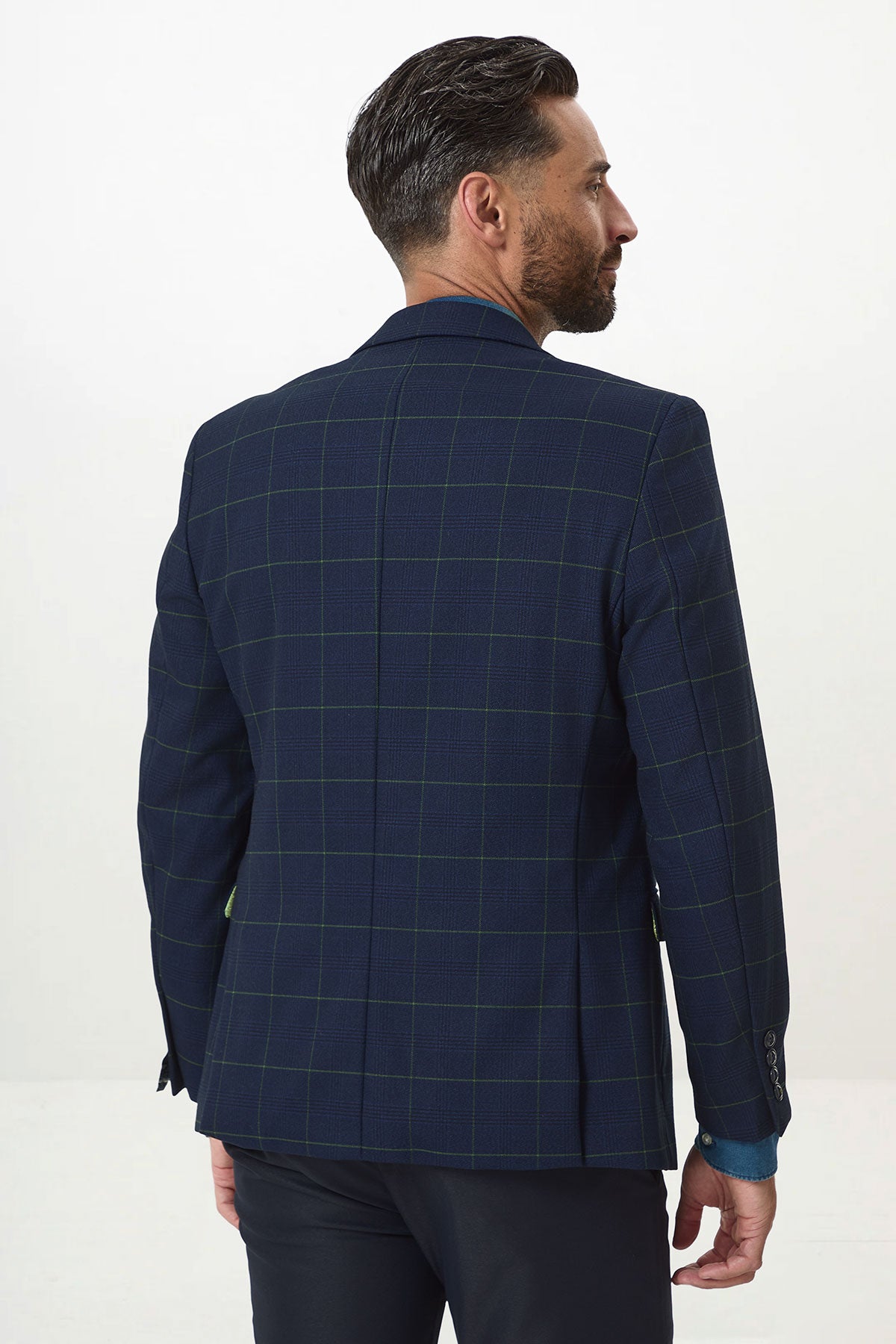 A man with short, dark hair and a beard faces away, wearing the Marc Darcy EDINSON Navy Green Check Blazer in a slim fit and dark trousers, standing against a plain white background.