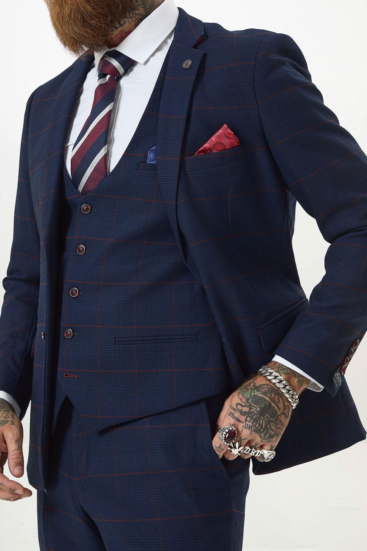 A man wears the Marc Darcy EDINSON Navy Wine Check Three Piece Suit with a red and navy striped tie, white shirt, and red pocket square. Tattooed hands adorned with rings and bracelets are visible; only his torso and lower face are shown.