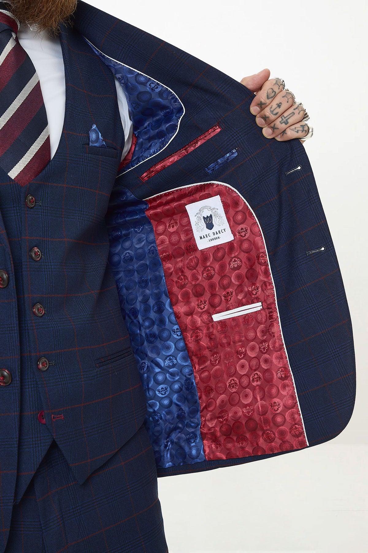 A person in the Marc Darcy EDINSON Navy Check Suit with Kelvin Wine Waistcoat opens their jacket to reveal a vibrant inner lining featuring blue and red satin panels with a circular pattern and a visible label.
