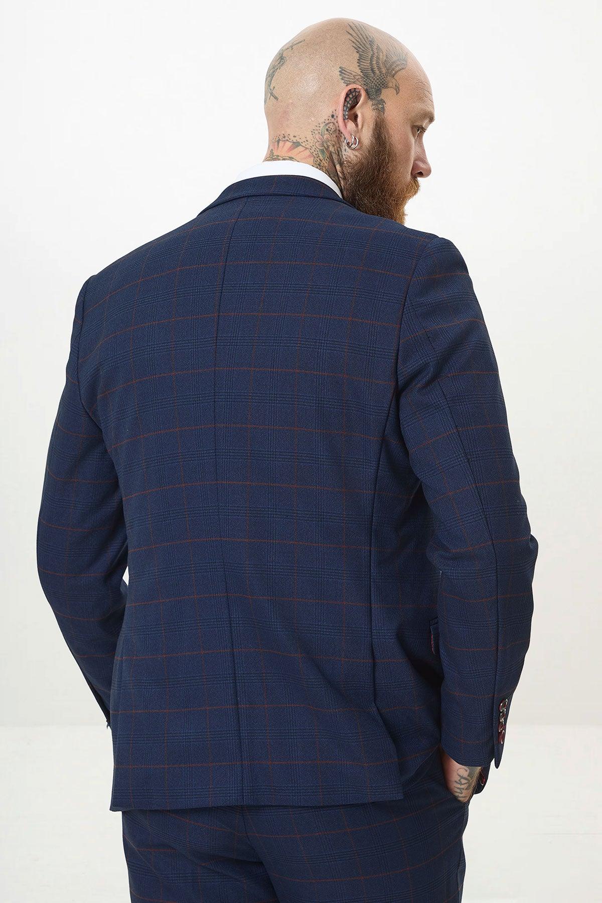 A man with a shaved head and tattoos models the Marc Darcy EDINSON Navy Check Suit with Kelvin Wine Waistcoat, standing against a plain white background, his right hand in his pocket as he faces away and looks to the side.