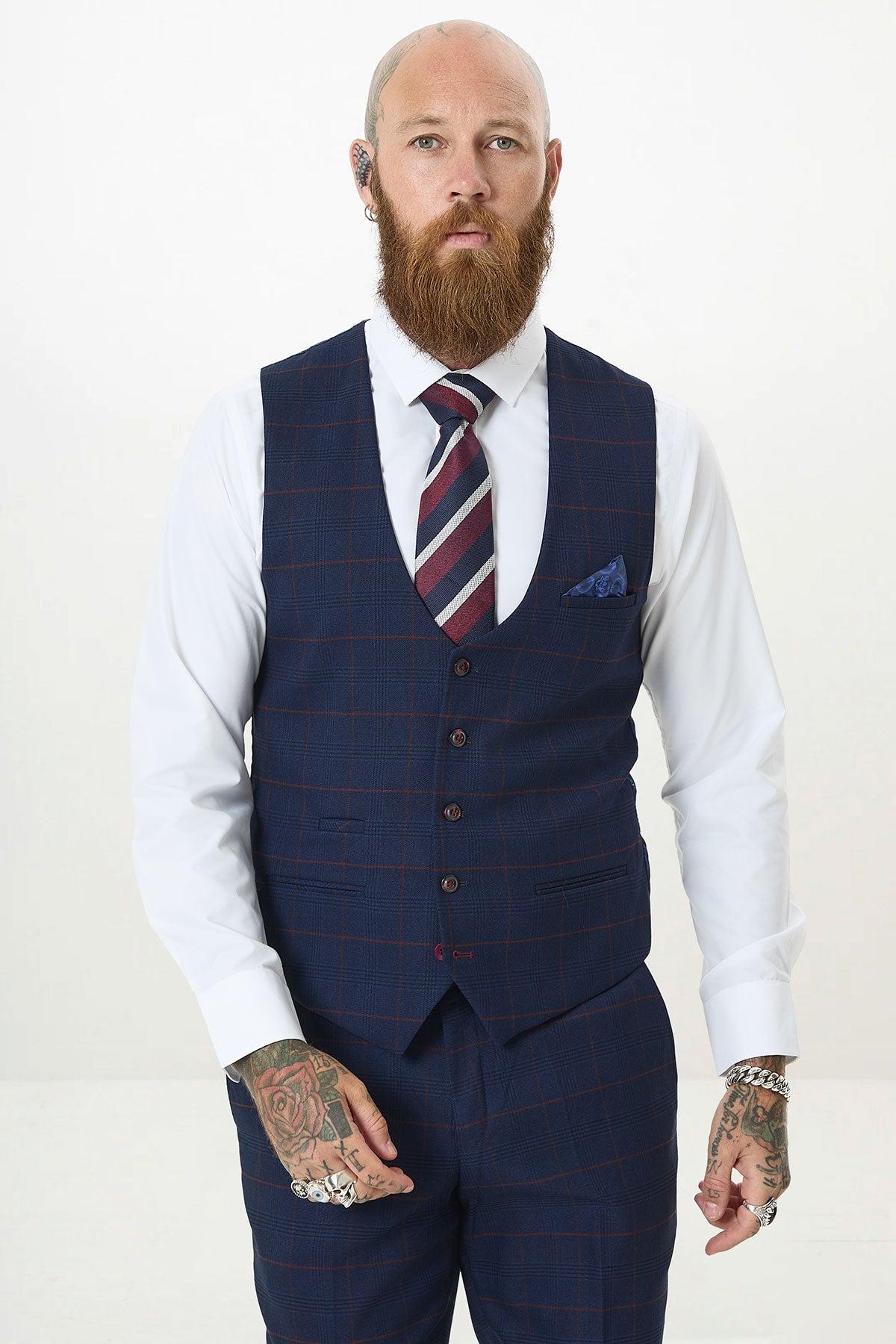 A bald, bearded, tattooed man wears a blue check Marc Darcy suit with a white shirt, striped tie, and the EDINSON Navy Wine Check Single Breasted Waistcoat.