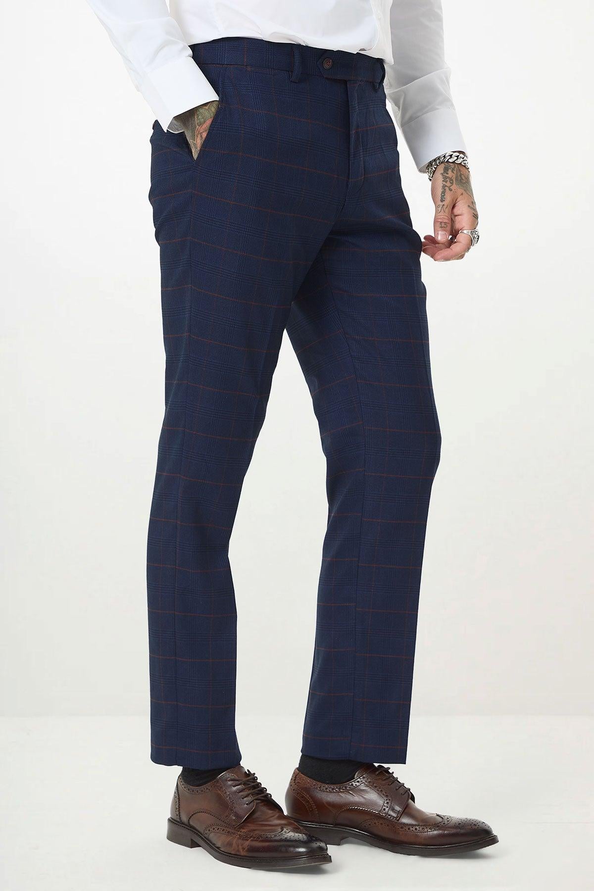 A man wears the Marc Darcy EDINSON Navy Wine Check Three Piece Suit in a slim tailored fit, paired with a white shirt, brown dress shoes, and socks, with one hand in his pocket.