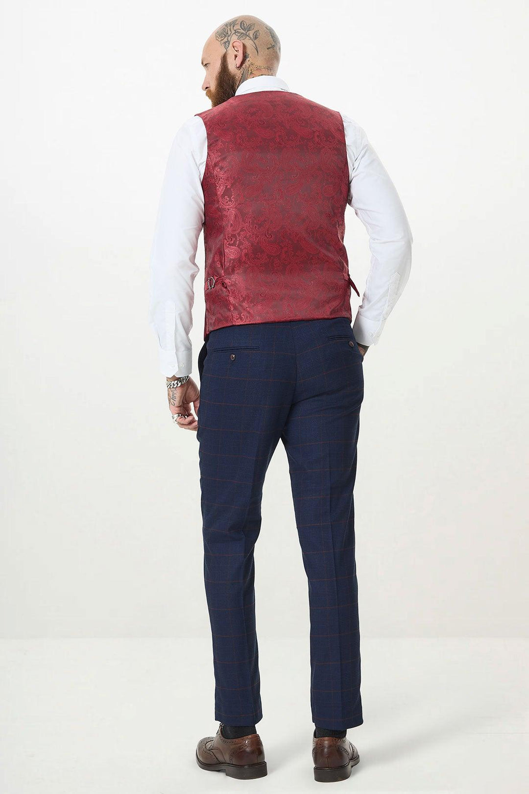 A tattooed man stands with his back to the camera in a white shirt, marcdarcys KELVIN Wine Single Breasted Waistcoat, navy checkered trousers, and brown shoes.